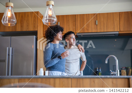 Two men standing behind wooden island in modern kitchen drinking water from clear glasses Two men standing behind wooden island in modern kitchen drinking water from clear glasses 141542212