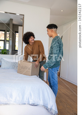 Two African American men arranging donation box on bed with white linens in bedroom with mirror Two African American men arranging donation box on bed with white linens in bedroom with mirror 141542217