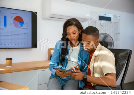 African American coworkers in business attire collaborating on tablet at office desk with monitor African American coworkers in business attire collaborating on tablet at office desk with monitor 141542224
