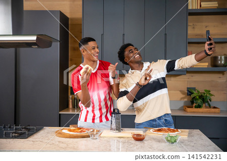 Diverse male friends preparing pizza dough and taking selfie in home kitchen with basil leaves Diverse male friends preparing pizza dough and taking selfie in home kitchen with basil leaves 141542231