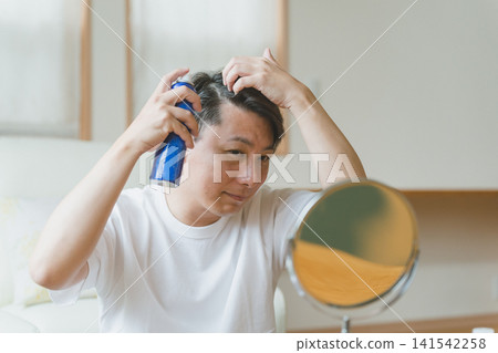 一名四十多歲的男子往頭上和頭髮上噴灑噴霧。 一名四十多歲的男子往頭上和頭髮上噴灑噴霧。 141542258