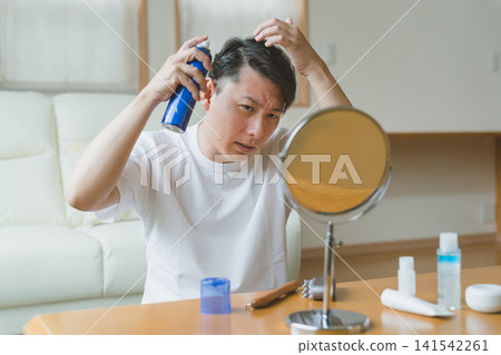 A man in his 40s frowns as he sprays hair growth spray. A man in his 40s frowns as he sprays hair growth spray. 141542261