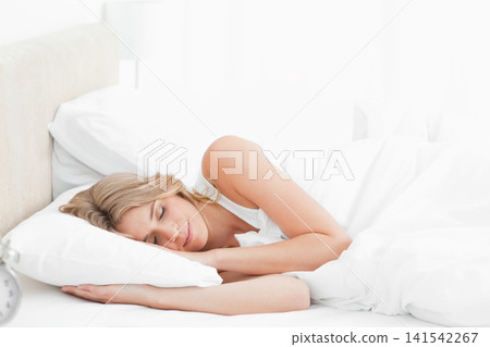 Woman lying on right side in bedroom with white pillow duvet and silver alarm clock Woman lying on right side in bedroom with white pillow duvet and silver alarm clock 141542267