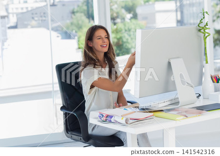 Woman sitting at white desk in modern office, working on desktop monitor with keyboard and mouse Woman sitting at white desk in modern office, working on desktop monitor with keyboard and mouse 141542316