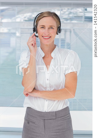 Mature adult female rep standing in office by window blinds adjusting headset, wearing white blouse Mature adult female rep standing in office by window blinds adjusting headset, wearing white blouse 141542320