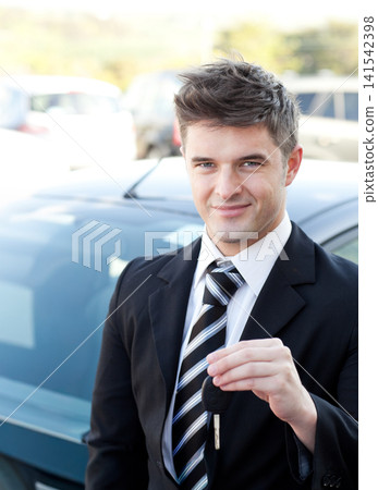 Man wearing suit and striped tie standing beside dark sedan at dealership lot holding key fob Man wearing suit and striped tie standing beside dark sedan at dealership lot holding key fob 141542398
