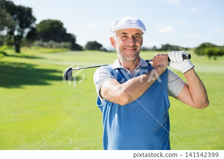 Senior male standing on golf fairway holding golf club, wearing white cap, glove, vest, smiling Senior male standing on golf fairway holding golf club, wearing white cap, glove, vest, smiling 141542399