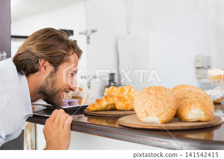 Man leaning over wooden counter smelling croissants on round boards, gripping edge, copy space Man leaning over wooden counter smelling croissants on round boards, gripping edge, copy space 141542415