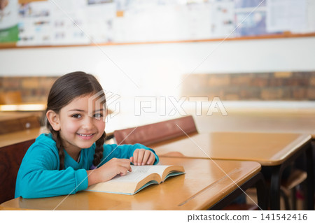 Child female student sitting in classroom at desk reading book, wearing turquoise top, copy space Child female student sitting in classroom at desk reading book, wearing turquoise top, copy space 141542416