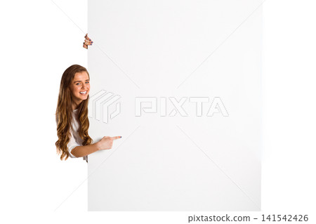 Woman peeking left in studio, pointing at blank white panel in white long-sleeve top, copy space Woman peeking left in studio, pointing at blank white panel in white long-sleeve top, copy space 141542426