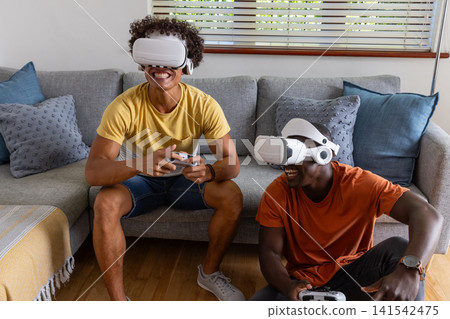 Diverse male friends playing vr games wearing headsets, controllers in living room Diverse male friends playing vr games wearing headsets, controllers in living room 141542475