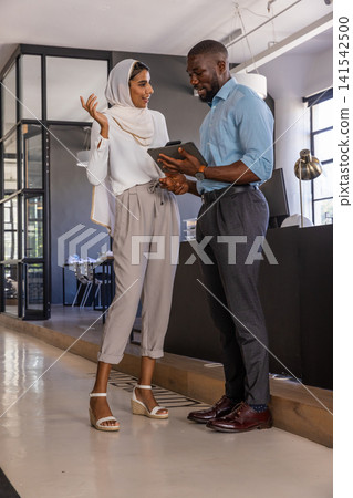 Diverse coworkers holding tablet and discussing report next to monitor by glass partition in office 141542500
