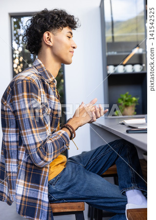 Hispanic man sitting on wooden stool at home desk rubbing hands near notebook and pen Hispanic man sitting on wooden stool at home desk rubbing hands near notebook and pen 141542525