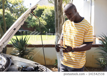 African american man wearing shirt cleaning engine under car hood in driveway, copy space African american man wearing shirt cleaning engine under car hood in driveway, copy space 141542538
