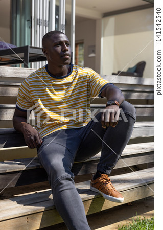 African american man sitting on house steps wearing shirt, wristwatch by glass door blinds African american man sitting on house steps wearing shirt, wristwatch by glass door blinds 141542540