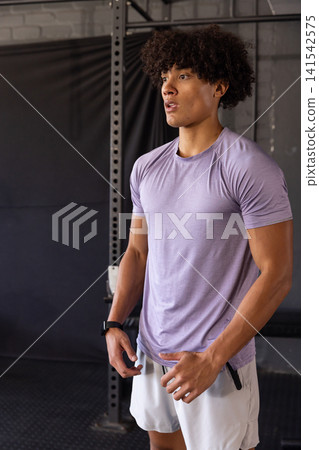 African American male athlete in sportswear posing by squat rack on gym floor with fitness tracker African American male athlete in sportswear posing by squat rack on gym floor with fitness tracker 141542575