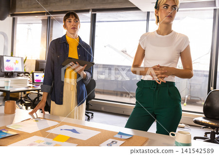 Female coworkers holding tablet and discussing color swatches and sketches in office Female coworkers holding tablet and discussing color swatches and sketches in office 141542589
