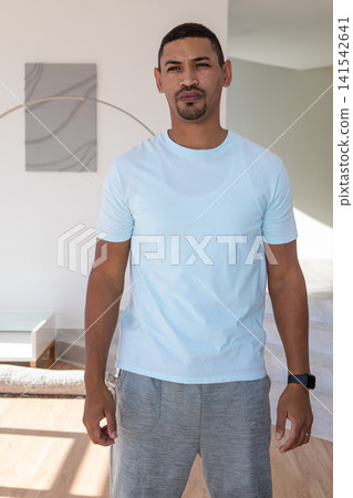 Mid-adult African American man standing by abstract artwork at home checking smartwatch, copy space Mid-adult African American man standing by abstract artwork at home checking smartwatch, copy space 141542641