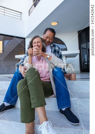 Senior couple sitting on marble steps outside building, holding ceramic mugs Senior couple sitting on marble steps outside building, holding ceramic mugs 141542642