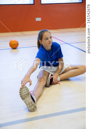 Female child in sneakers stretching and reaching foot on gym floor near ball Female child in sneakers stretching and reaching foot on gym floor near ball 141542676