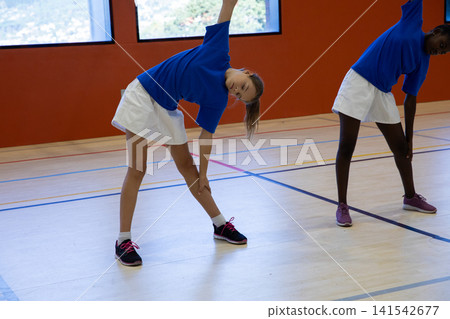 Diverse female students performing side stretches on gym court under windows, copy space Diverse female students performing side stretches on gym court under windows, copy space 141542677