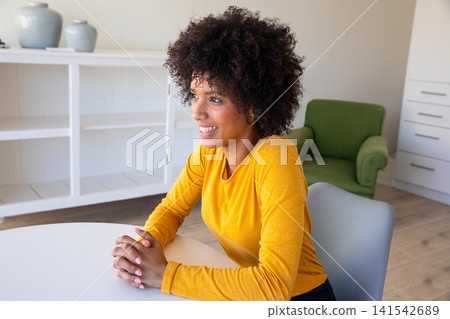 Smiling african american woman in yellow top at table at home, looking to right 141542689