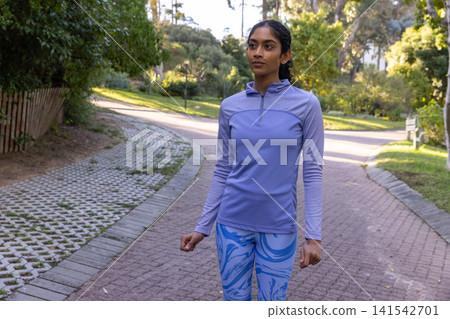 Asian indian woman standing on winding brick path in park wearing pullover, blue leggings Asian indian woman standing on winding brick path in park wearing pullover, blue leggings 141542701