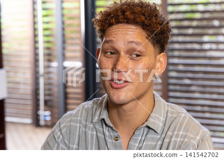 Man sitting in lounge room wearing grey shirt and engaging in conversation by wooden blinds 141542702