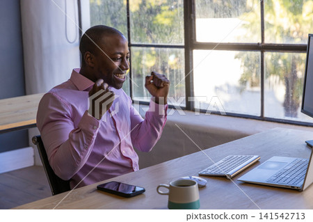 African american man celebrating at office desk with laptop keyboard copy space African american man celebrating at office desk with laptop keyboard copy space 141542713