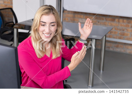 Businesswoman wearing pink blouse sitting at desk typing on computer in meeting room, copy space Businesswoman wearing pink blouse sitting at desk typing on computer in meeting room, copy space 141542735