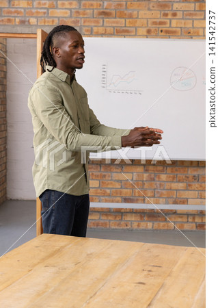 African american man in olive shirt presenting on whiteboard next to table in meeting room 141542737