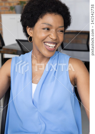 African American woman sitting on mesh office chair at desk smiling and looking left African American woman sitting on mesh office chair at desk smiling and looking left 141542738