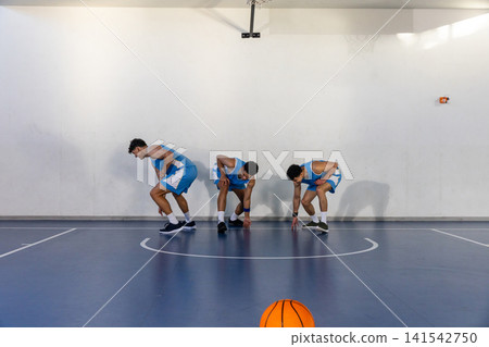 Three african american men in uniforms squatting under hoop on court with orange basketball 141542750