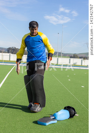 Asian indian teenage male goalkeeper striding on turf field with leg guards and helmet, kicking pad Asian indian teenage male goalkeeper striding on turf field with leg guards and helmet, kicking pad 141542767