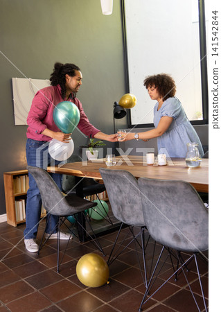 African american couple decorating table with metallic balloons while handing glass, dining room African american couple decorating table with metallic balloons while handing glass, dining room 141542844