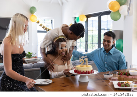 Diverse friends gathering at dining table at home celebrating birthday, happy birthday 21 cake Diverse friends gathering at dining table at home celebrating birthday, happy birthday 21 cake 141542852