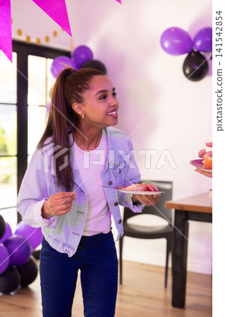 Asian teenage female holding paper plate with cake slice in party room with balloons, banner Asian teenage female holding paper plate with cake slice in party room with balloons, banner 141542854