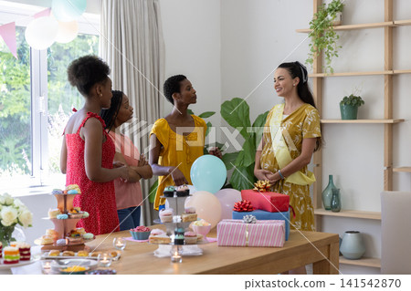 Diverse female friends gathering around table in dining area with cupcakes and candles, copy space Diverse female friends gathering around table in dining area with cupcakes and candles, copy space 141542870