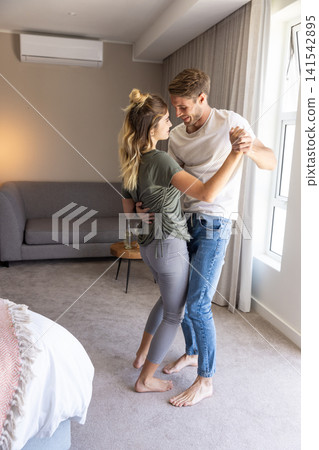 Couple dancing barefoot on grey carpet beside side table with glass bottle in bedroom 141542895