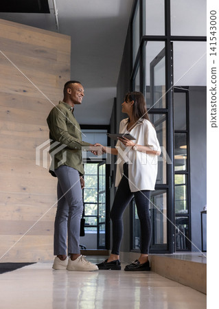 Diverse coworkers shaking hands in office holding tablet and wearing business attire Diverse coworkers shaking hands in office holding tablet and wearing business attire 141543000