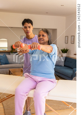 Senior woman client and trainer lifting orange dumbbells on bench in living room guiding posture Senior woman client and trainer lifting orange dumbbells on bench in living room guiding posture 141543012