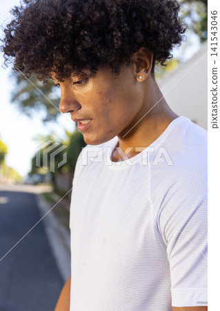 African american man pausing on suburban street wearing white mesh athletic shirt, stud earring 141543046