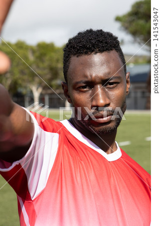 African American man standing on sports field extending arm at camera wearing red and white jersey African American man standing on sports field extending arm at camera wearing red and white jersey 141543047