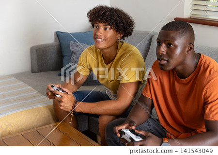 Two male friends holding controllers while gaming on gray couch in living room Two male friends holding controllers while gaming on gray couch in living room 141543049
