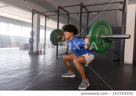 African American man performing barbell back squat on rubber mat in gym by racks, copy space African American man performing barbell back squat on rubber mat in gym by racks, copy space 141543050
