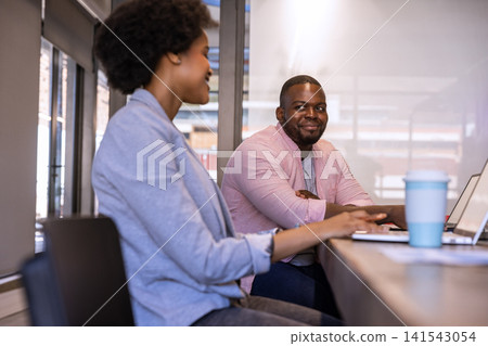 African american colleagues sitting in office discussing project using laptops with mug African american colleagues sitting in office discussing project using laptops with mug 141543054