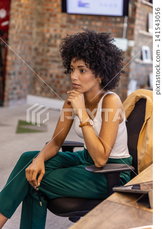 African american woman resting chin at office desk and chair with laptop monitors African american woman resting chin at office desk and chair with laptop monitors 141543056