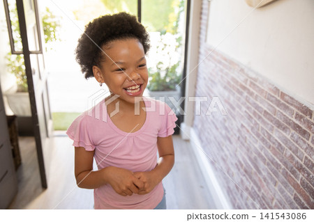 Smiling African American girl standing in entryway wearing pink shirt seeing garden via glass door Smiling African American girl standing in entryway wearing pink shirt seeing garden via glass door 141543086