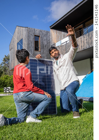South asian father and son kneeling by solar panel, pointing next to camping tent and patio chairs South asian father and son kneeling by solar panel, pointing next to camping tent and patio chairs 141543146