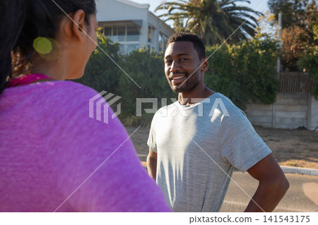 Diverse friends pausing mid run and chatting on suburban sidewalk by hedge Diverse friends pausing mid run and chatting on suburban sidewalk by hedge 141543175